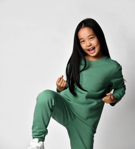 Excited asian preteen girl in green clothing showing yes gesture - Foto, afbeelding