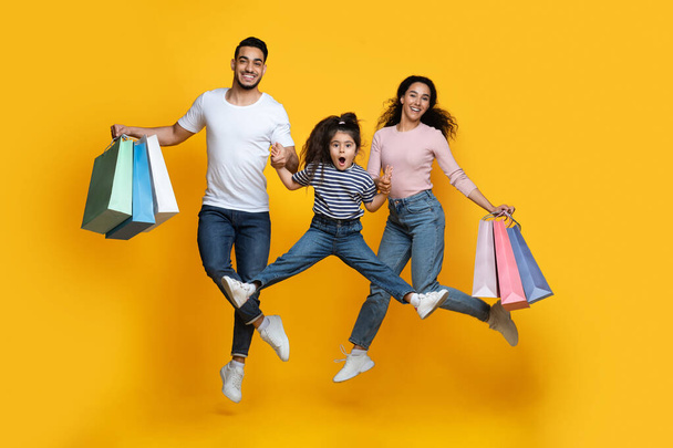 Seasonal Sales. Happy Middle Eastern Family Of Three Jumping With Shopping Bags - Foto, Imagen
