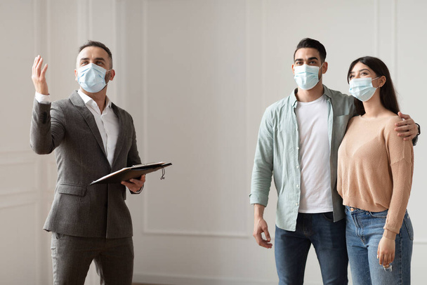 Agente imobiliário em máscara médica mostrando compradores novo apartamento - Foto, Imagem