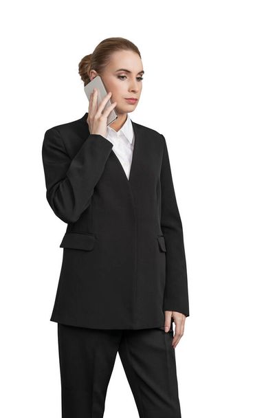 Business Woman in black suit with smartphone calling, standing pensive. Isolated on white background. Concept of business consulting and advisory - Фото, изображение