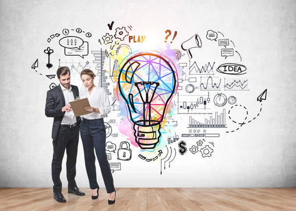 Businessman and businesswoman in formal clothes holding clipboard and brainstorming nearby concrete wall with colorful business idea lightbulb sketch. Concept of creativity and start up. Full length - Foto, immagini