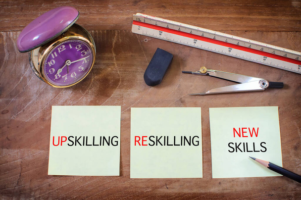 Up skilling, reskilling and new skills written on sticky notes with alarm clock on wooden table. Business self improvement concept and sustainable development idea - Photo, Image