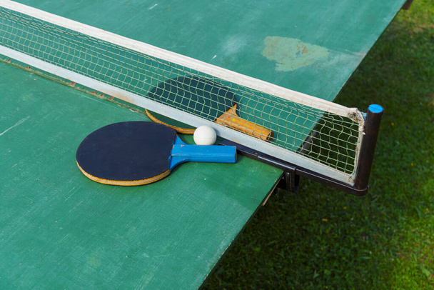 Raquetas viejas y pelota de ping pong en el borde de la mesa al aire libre en verano - Foto, Imagen