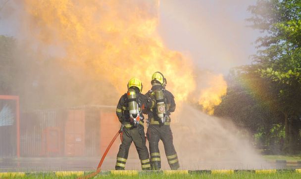 A group of firefighter or fireman with uniform using water fire hose against hot burning fire and dangerous smoke in the container, an emergency accident rescue. People. Hero teamwork. - Fotografie, Obrázek