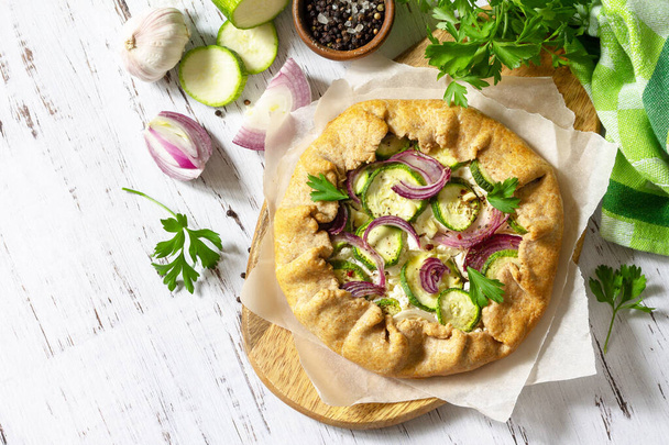 Healthy rye flour baked goods, gluten free, diet food. Galette with zucchini, onions and feta cheese on a wooden table. Top view flat lay background. Copy space. - Foto, Bild