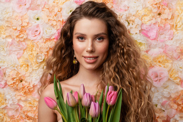 Half-naked young woman smiling while posing with tulips isolated over flowers background - Фото, зображення
