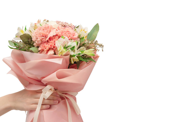 Μπουκέτο με απαλά ροζ λουλούδια σε ροζ χαρτί περιτυλίγματος σε γυναικεία χέρια που απομονώνονται σε λευκό φόντο. - Φωτογραφία, εικόνα