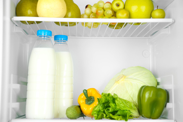 Milk bottles, vegetables and fruits in open refrigerator. Weight loss diet concept. - Фото, зображення