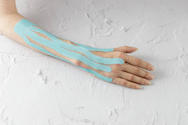 Frauenhand mit blauen medizinischen Flecken aus elastischem Kinesioband zum Schutz vor Ödemen in der postoperativen Phase und während der Rehabilitation auf weißem Tisch - Foto, Bild