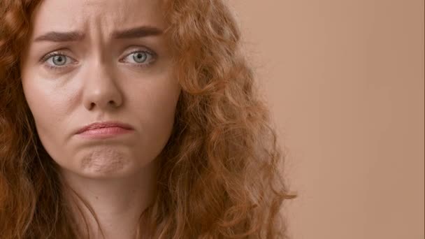 Traurige rothaarige Frau blickt frustriert in die Kamera, beiger Hintergrund - Filmmaterial, Video