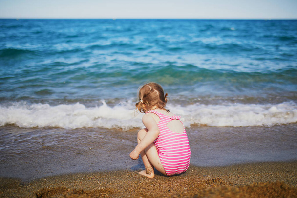 Happy little girl having fun on the beach at Mediterranean sea in France. Cheerful kid enjoying vacation at the sea. Outdoor summer activities for children - Photo, Image