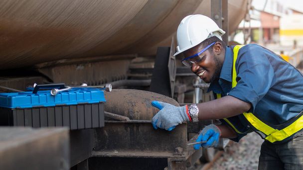 Africký strojní technik v helmě, hájích a záchranné vestě používá klíč k opravě plynu a oleje pro přepravu vlaků - Fotografie, Obrázek