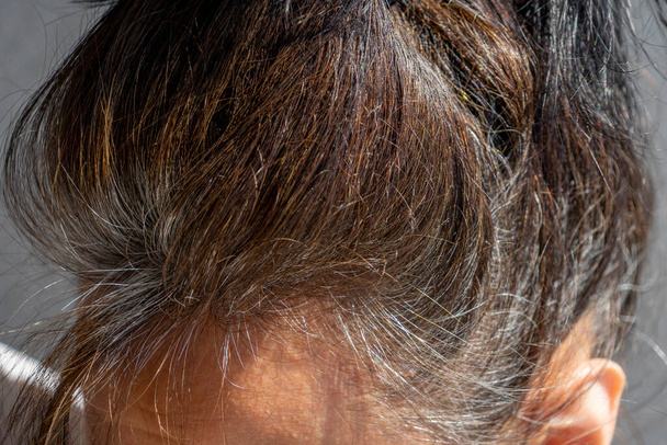 Close-up van middelbare leeftijd Kaukasische vrouw met donkerbruin haar en hergroeide grijze haarwortels - Foto, afbeelding