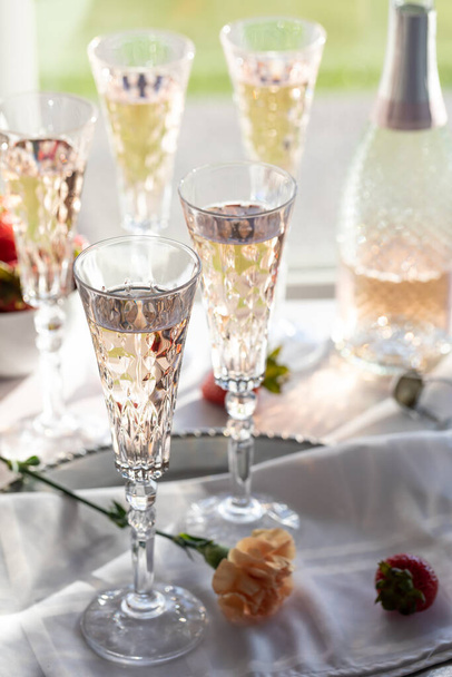 A vertical view of several tall crystal flute glasses filled with sparkling rose wine, back lit against a sunny window. - Fotó, kép