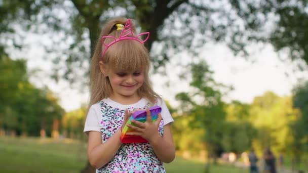 Μικρό κομψό κορίτσι παιδί παίζει πολύχρωμο squishy φυσαλίδες σιλικόνης αισθητηριακές ποπ παιχνίδι στο πάρκο - Πλάνα, βίντεο