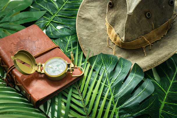 Travel Style Notebook with Compass and Hat, Green Tropical Leaves Background, Adventure Expedition Concept  - Photo, Image