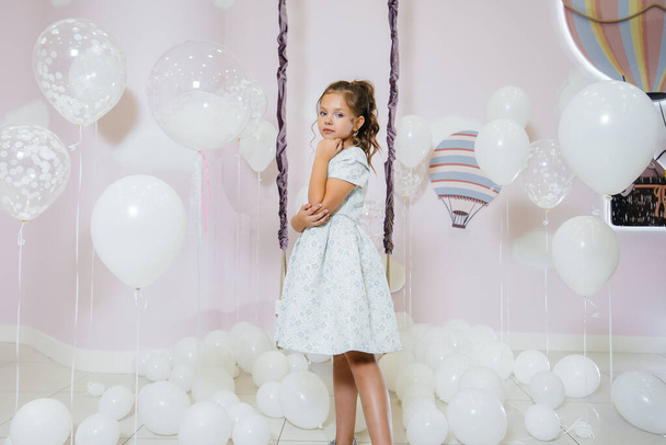 A little cute girl smiles and poses against the background of a swing with balloons. - Zdjęcie, obraz