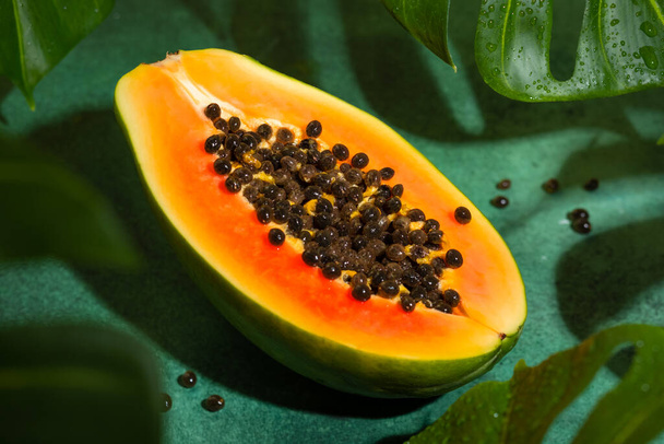 Fresh half of papaya with seeds on tropical leaves background. Tropical exotic fruit. - Photo, image