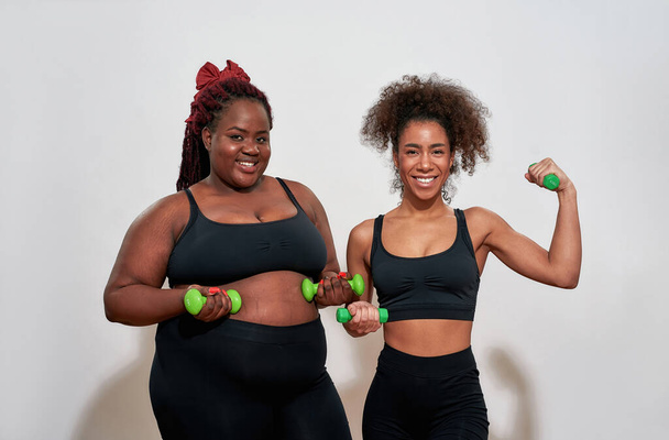 Picture of two afro women holding dumbbells and smiling in camera - Фото, зображення