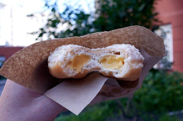 Ένα ντόνατ με κρέμα σε χάρτινο πακέτο. Επιδόρπιο για καφέ. - Φωτογραφία, εικόνα