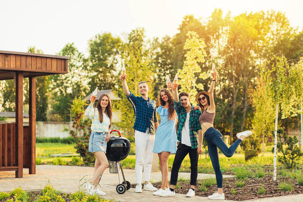 Group of young happy friends having barbecue party in nature, friends fry meat, chat and drink lemonade outdoors in summer - 写真・画像