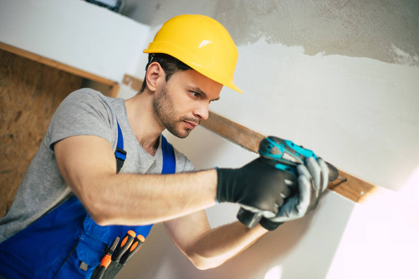 Young home repair male or worker busy with house renovation, holds building equipment, wears casual working clothes in the new build - Foto, Imagen