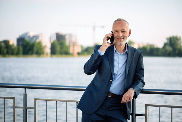 Lächelnder Geschäftsmann im grauen Anzug mit Smartphone. - Foto, Bild