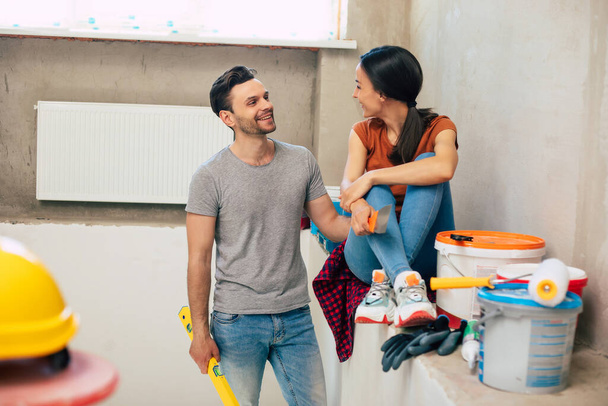 Modern happy young couple in love in casual clothes during new home repair or renovation of walls with a lot of tools for this - Foto, immagini