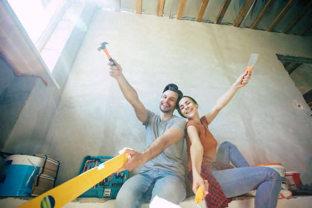 Modern happy young couple in love in casual clothes during new home repair or renovation of walls with a lot of tools for this - Foto, Imagem