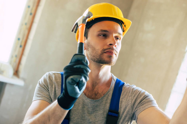 Young home repair male or worker busy with house renovation, holds building equipment, wears casual working clothes in the new build - Фото, изображение