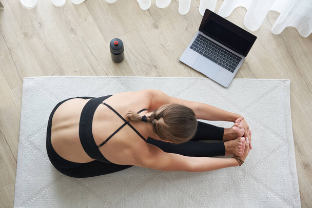 Top view of young woman practicing yoga, sitting in Seated forward bend exercise, paschimottanasana pose, working out, wearing sportswear - Photo, image