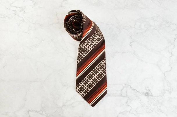 Brązowy krawat z geometrycznym wzorem na marmurowym tle. Kopiuj miejsce na tekst. - Zdjęcie, obraz