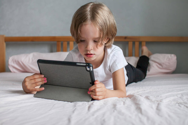 Küçük kız internette ödev yapıyor, evde yatakta yatıyor. Çevrimiçi akrabalarla iletişim. Yeni okul yılının başlangıcı konsepti. - Fotoğraf, Görsel