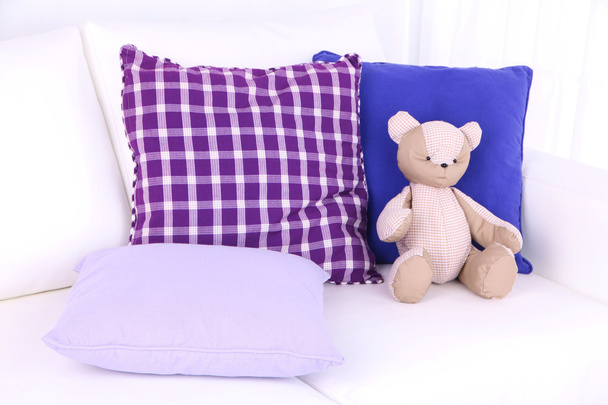 Медвежья игрушка с подушками на диване
 - Фото, изображение