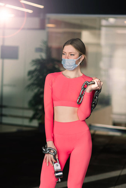 Coronavirus covid-19 prevención, fitness girl with a medical mask holding dumbbell, circuito de entrenamiento - Foto, imagen