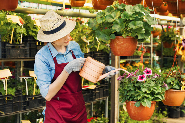 Jardineiro mulher em chapéu e luvas trabalha com flores na estufa. - Foto, Imagem