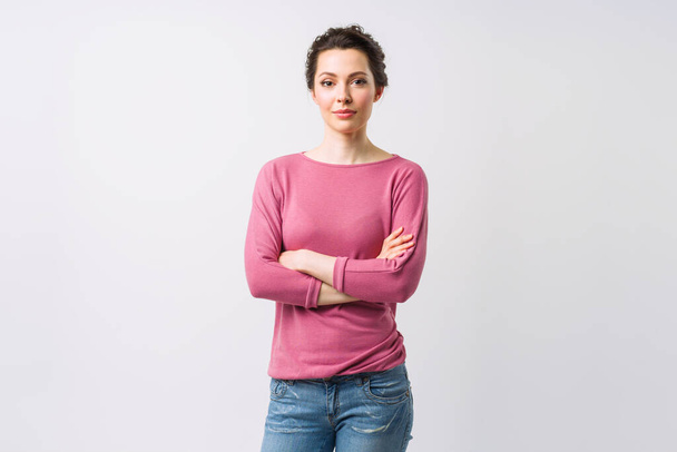 Jonge vrouw portret. Schattige brunette in een trui kijkend naar de camera met haar armen gekruist. - Foto, afbeelding