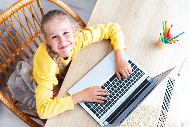 Caucasian girl sits at a desk, hands on laptop keyboard, smiles, top view. - Photo, Image