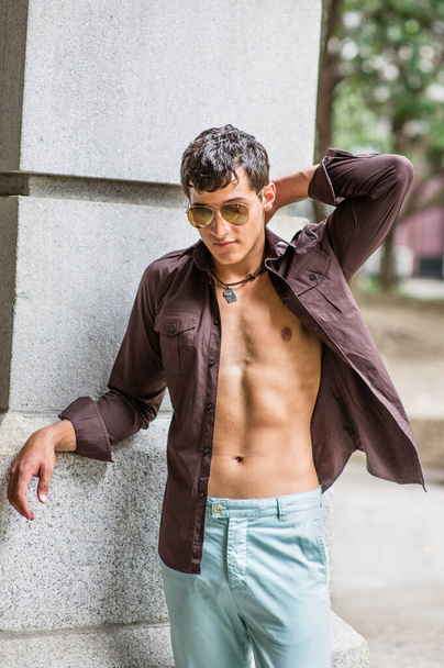 Wearing sunglasses, with his shirts unbuttoned, a young fellow is standing there, scratching the back of his head and taking a break - Foto, afbeelding