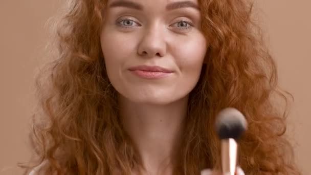 Mujer haciendo maquillaje aplicando polvo con cepillo cosmético, fondo beige - Metraje, vídeo