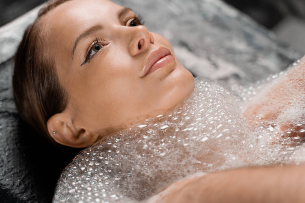 Close-up portrait of girl on foam peeling procedures in spa. Model is relaxing in Turkish hammam - Photo, Image