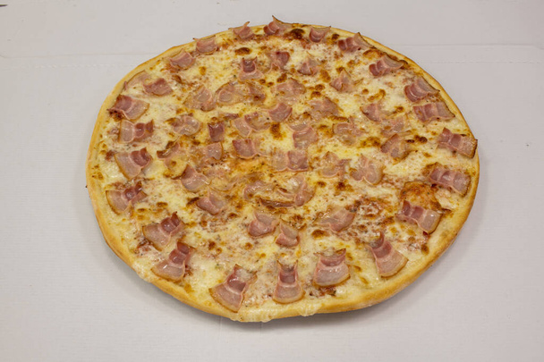große Pizza mit vielen gleich großen Speckstücken, die fast mathematisch auf den geschmolzenen Mozzarella-Käse und einen weißen Papphintergrund gelegt werden - Foto, Bild