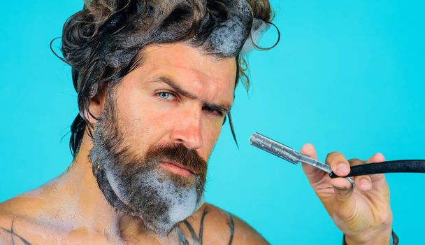 Bearded man shaving beard with straight razor in shower. Beard Care. Beauty, hygiene, grooming and people concept. - Photo, Image