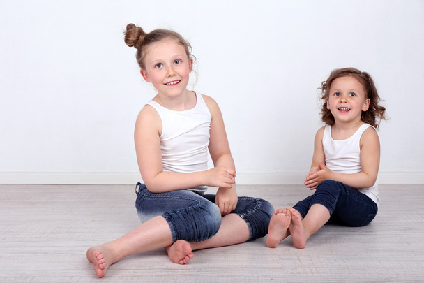 Beautiful small girls sitting on floor on wall background - 写真・画像