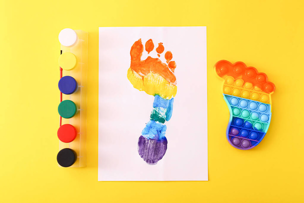 New trendy popular silicone colorful anti stress Pop It toy for child and colorful footprint on yellow background. - Foto, imagen