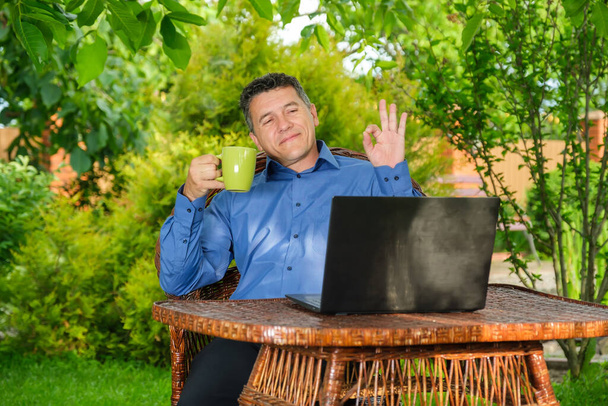 Man drinking coffee and showing ok sign to business partner via laptop - Photo, Image