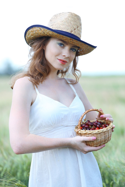 Beautiful young woman holding wicker basket with cherries in field - Foto, immagini