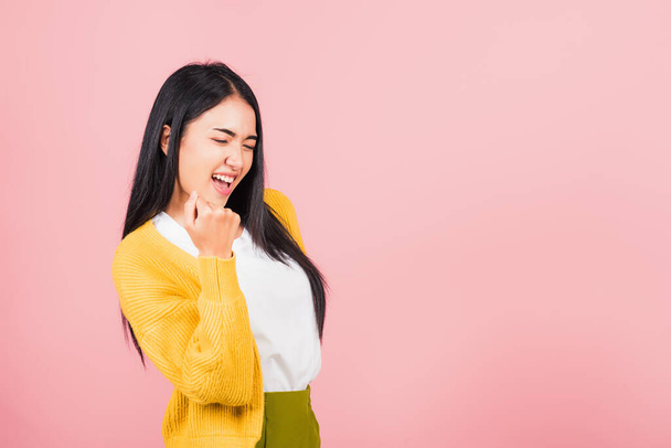 Happy Asian portrait beautiful cute young woman stand makes raised fists up celebrating her winning success gesture, studio shot isolated pink background, Thai female excited say yes! with copy space - Fotó, kép