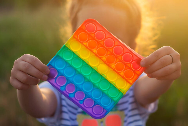 The child plays with a colorful rainbow game of poppit. Silicone fidget close-up - Photo, image