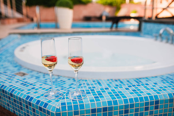 Dvě sklenice šampaňského s jahodami na slunné terase venkovní terasa s výhledem na bazén v letní den mimo město. Detailní pohled. - Fotografie, Obrázek